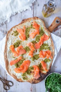 Flammkuchen mit Pesto und Lachs, daneben eine Sch&uuml;ssel mit Rucola.
