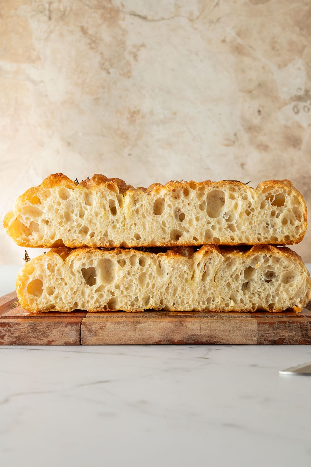 Aufgeschnittene Focaccia mit goldbrauner Kruste und luftiger, gro&szlig;poriger Krume auf einem Holzbrett.