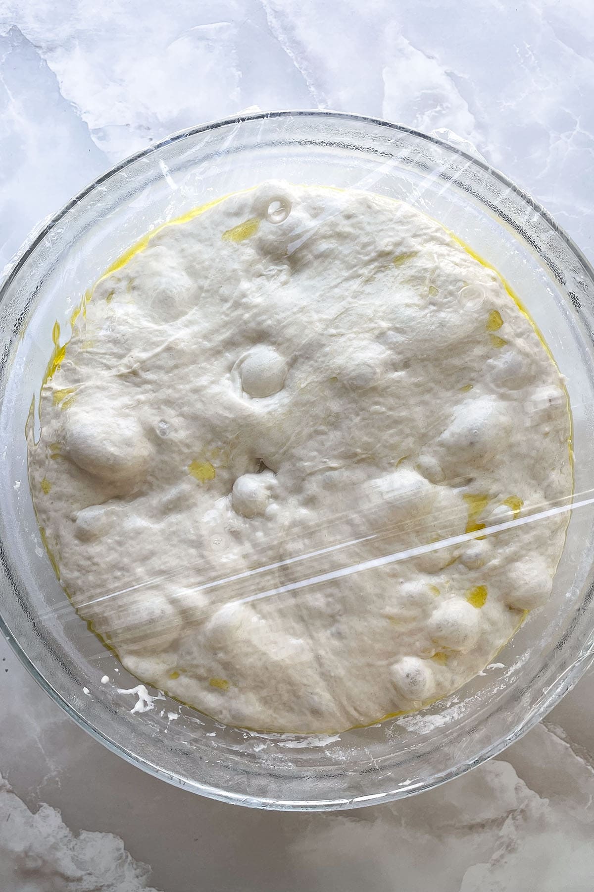 Luftig aufgegangener Focaccia-Teig mit sichtbaren Luftblasen und Oliven&ouml;l nach der Gehzeit im K&uuml;hlschrank.