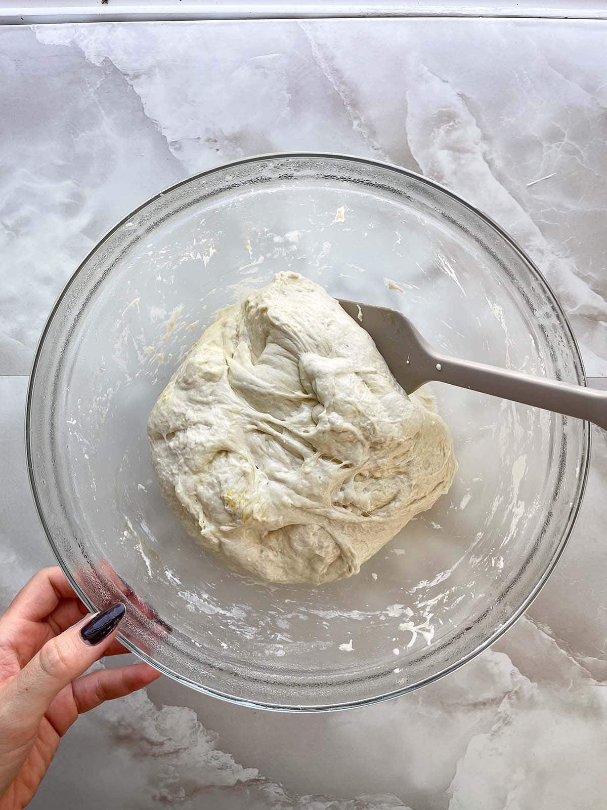 Focaccia-Teig wird nach dem Gehen mit einem Teigschaber von der Sch&uuml;ssel abgel&ouml;st.