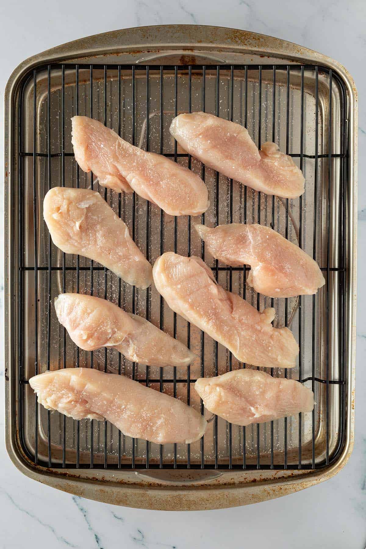 Gesalzene rohe H&auml;hnchenst&uuml;cke beim Dry Brining auf einem Gitter.
