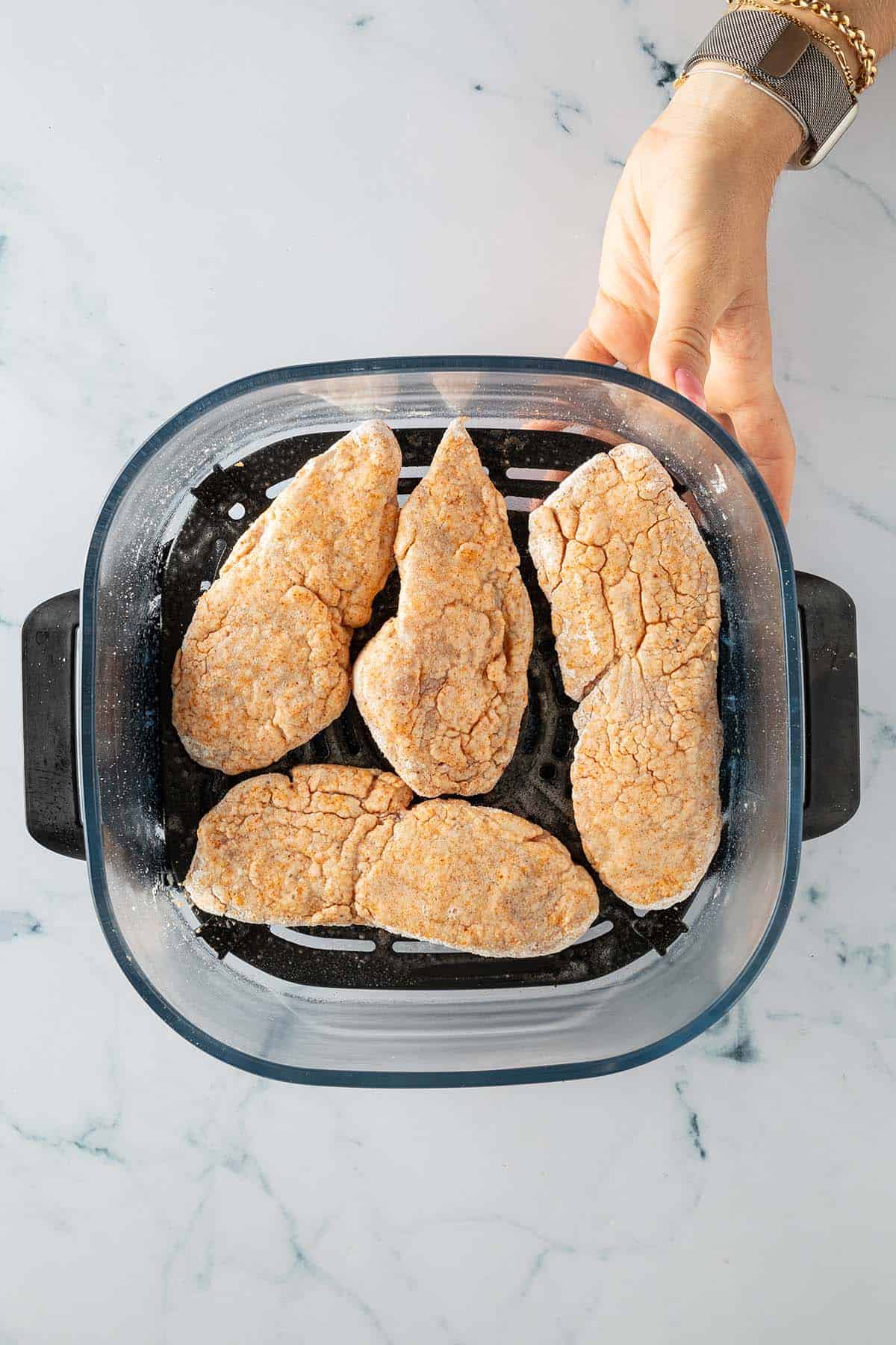 Panierte und einge&ouml;lte H&auml;hnchenst&uuml;cke vor dem Backen im Korb des Airfryers.