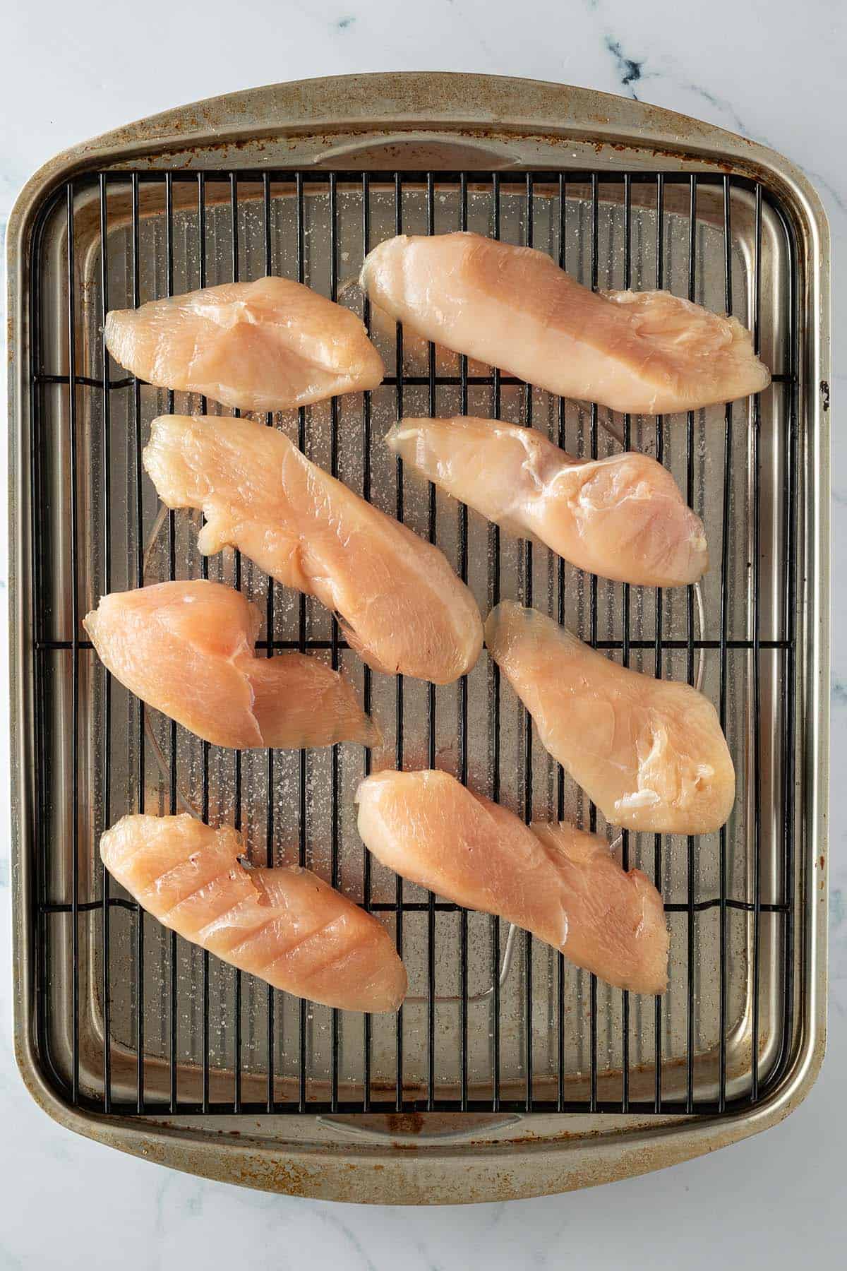 Rohe H&auml;hnchenst&uuml;cke auf einem Gitter nach dem Dry Brining im K&uuml;hlschrank.