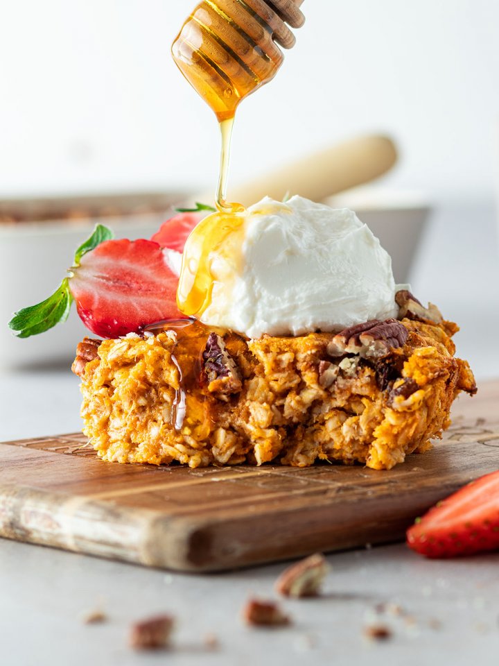Ein St&uuml;ck Haferflockenauflauf mit Erdbeeren und Joghurt on top, auf dem Honig getr&auml;ufelt wird.