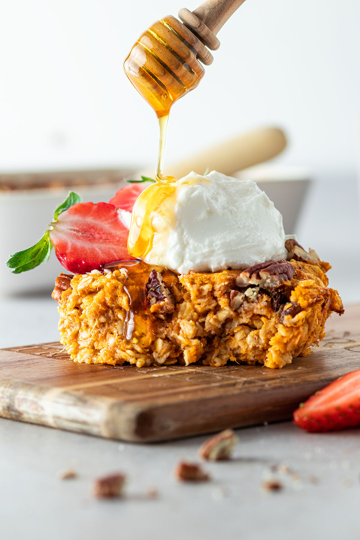 Ein St&uuml;ck Haferflockenauflauf mit Erdbeeren und Joghurt on top, auf dem Honig getr&auml;ufelt wird.