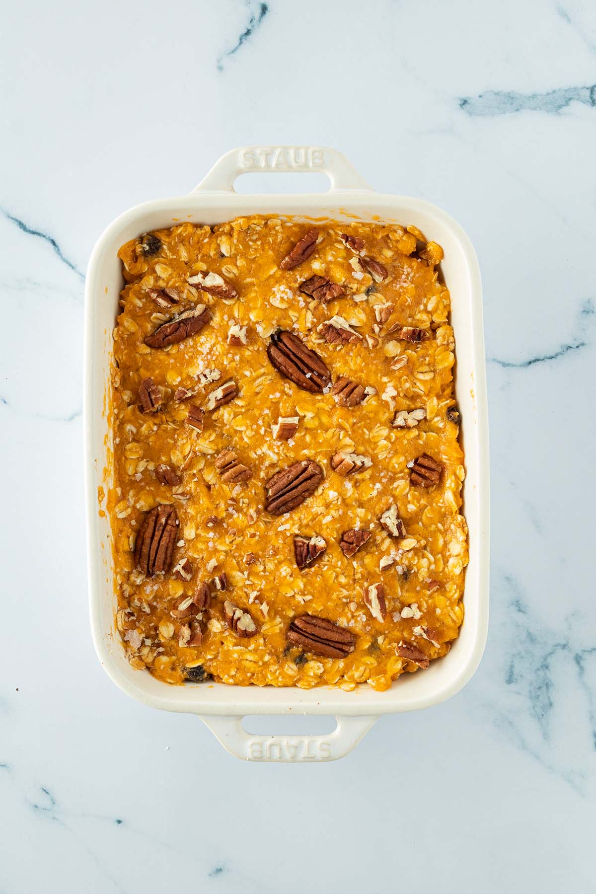 Fr&uuml;hst&uuml;cksauflauf vor dem Backen in einer Auflaufform mit ganzen und zerkleinerten N&uuml;ssen auf der Oberfl&auml;che.