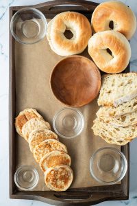Leere Sch&uuml;sseln, Bagels, Brot und Pfannkuchen wurden auf dem Holzbrett verteilt.