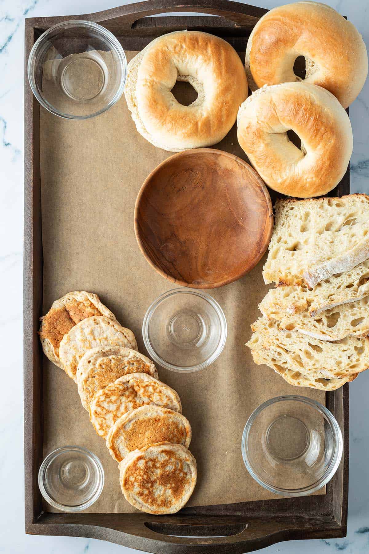 Leere Sch&uuml;sseln, Bagels, Brot und Pfannkuchen wurden auf dem Holzbrett verteilt.