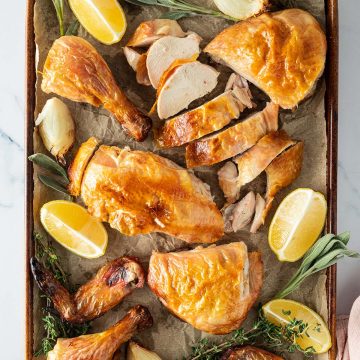 Ganzes H&auml;hnchen aus dem Backofen aufgeschnitten auf einem Blech mit Zitronenspalten, Zwiebeln und frischen Kr&auml;utern.