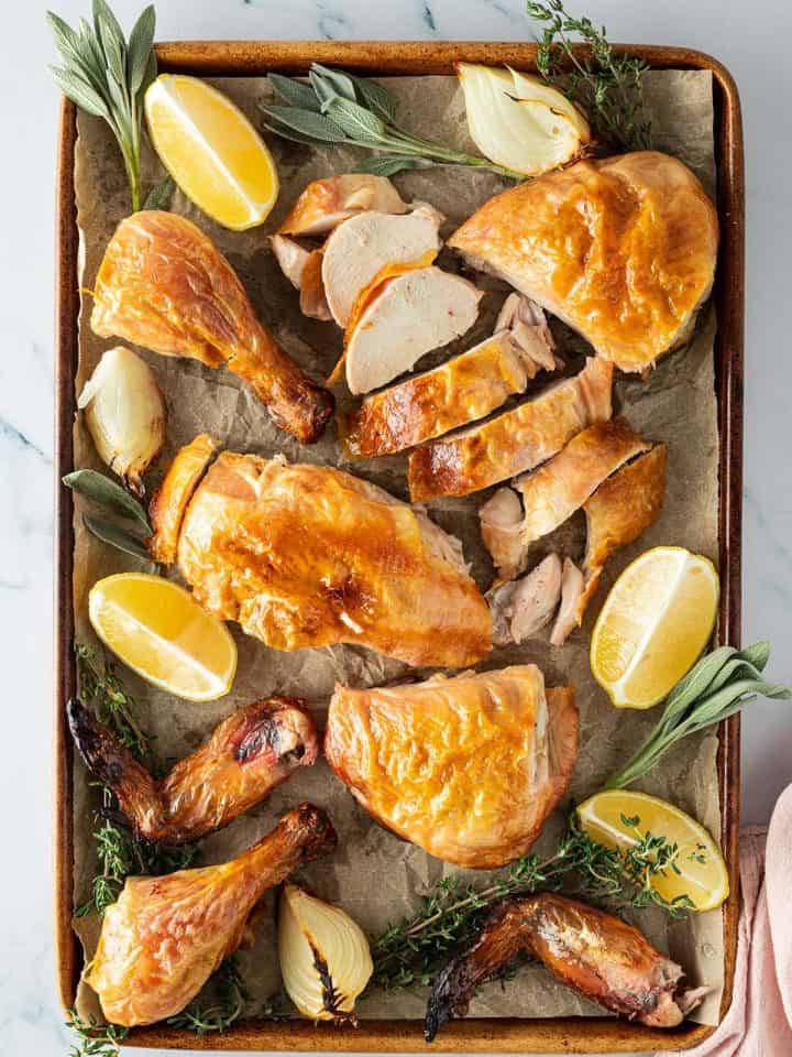 Ganzes H&auml;hnchen aus dem Backofen aufgeschnitten auf einem Blech mit Zitronenspalten, Zwiebeln und frischen Kr&auml;utern.