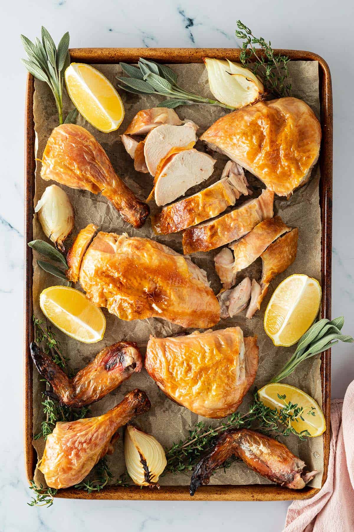 Ganzes H&auml;hnchen aus dem Backofen aufgeschnitten auf einem Blech mit Zitronenspalten, Zwiebeln und frischen Kr&auml;utern.
