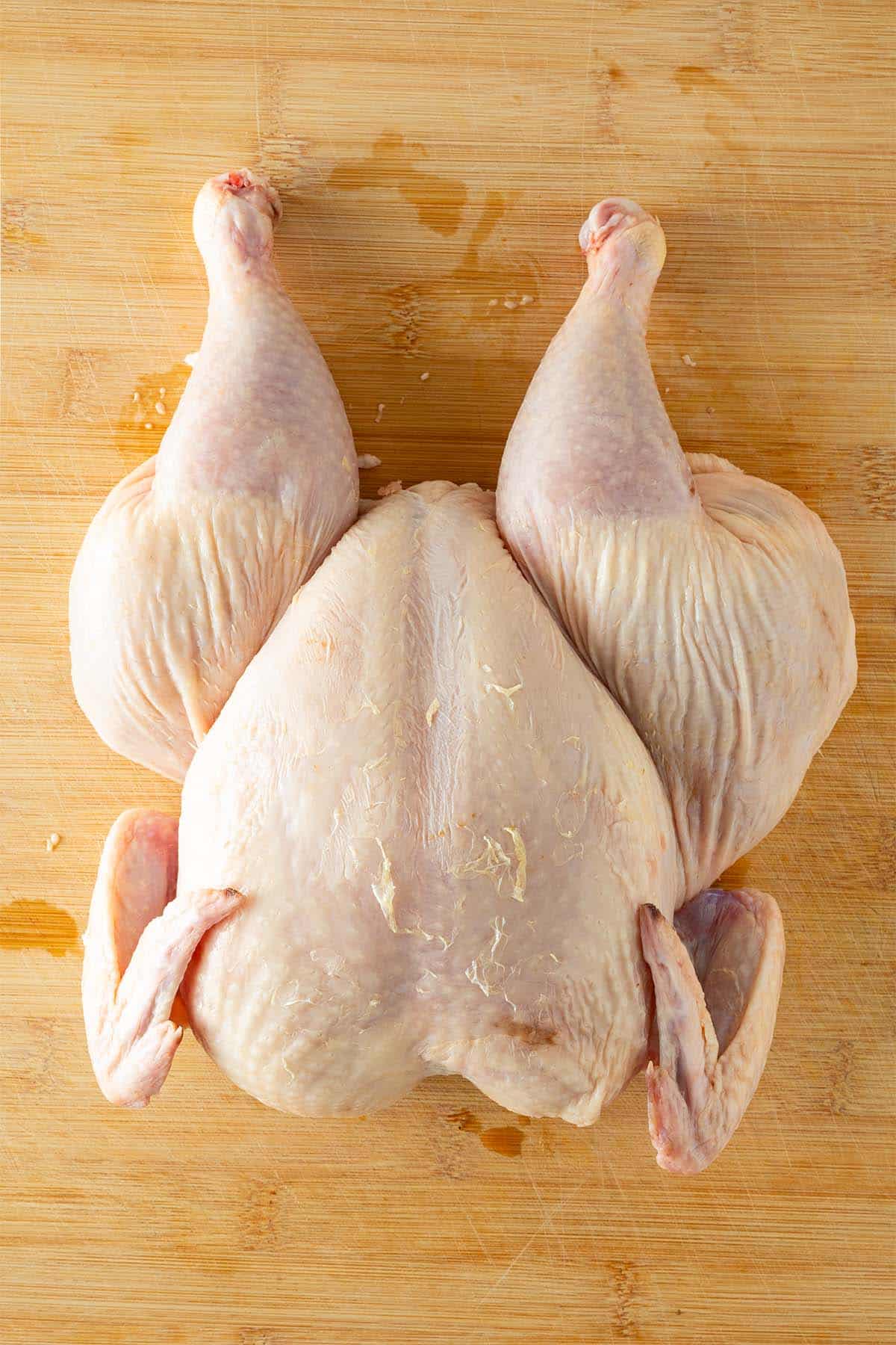 Ganzes, rohes H&auml;hnchen auf einem Holzbrett mit entferntem R&uuml;ckgrat.