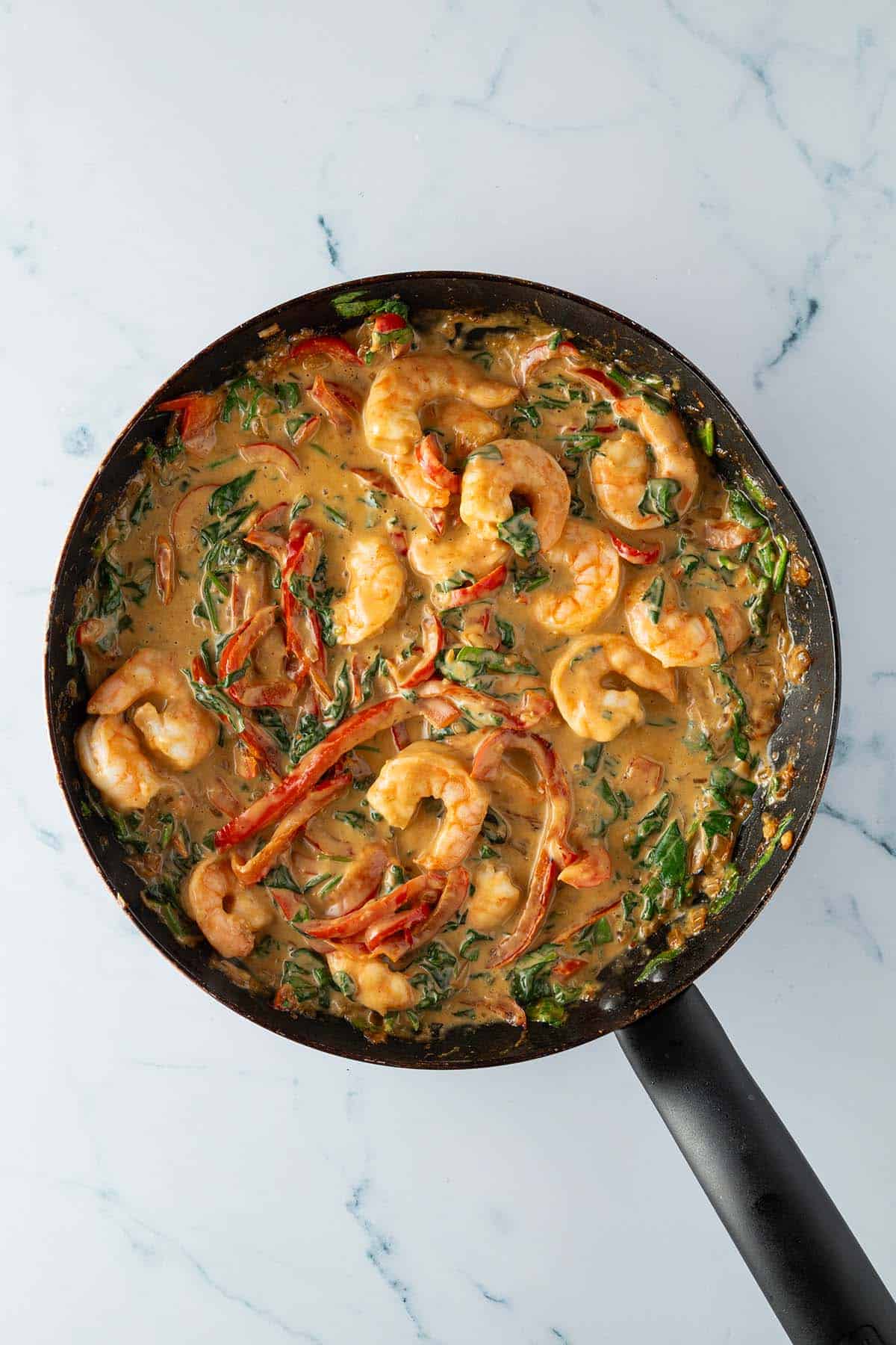 Thai Curry mit Garnelen, Spinat und Kokosmilch in einer Pfanne.