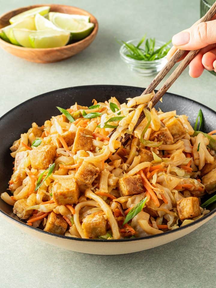 Jemand nimmt mit Essst&auml;bchen einen Bissen gebratene Udon Nudeln in die Hand.