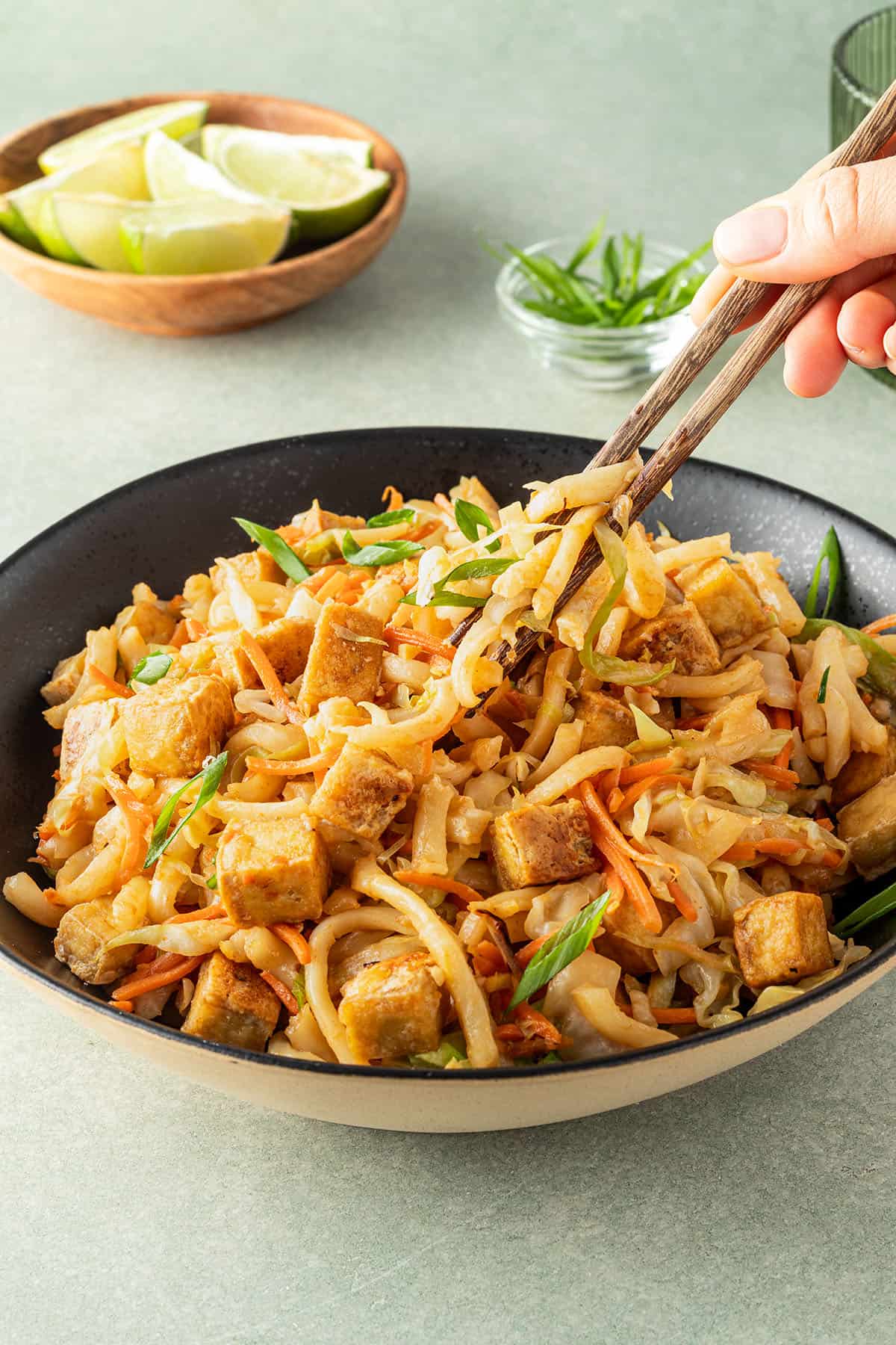 Jemand nimmt mit Essst&auml;bchen einen Bissen gebratene Udon Nudeln in die Hand.