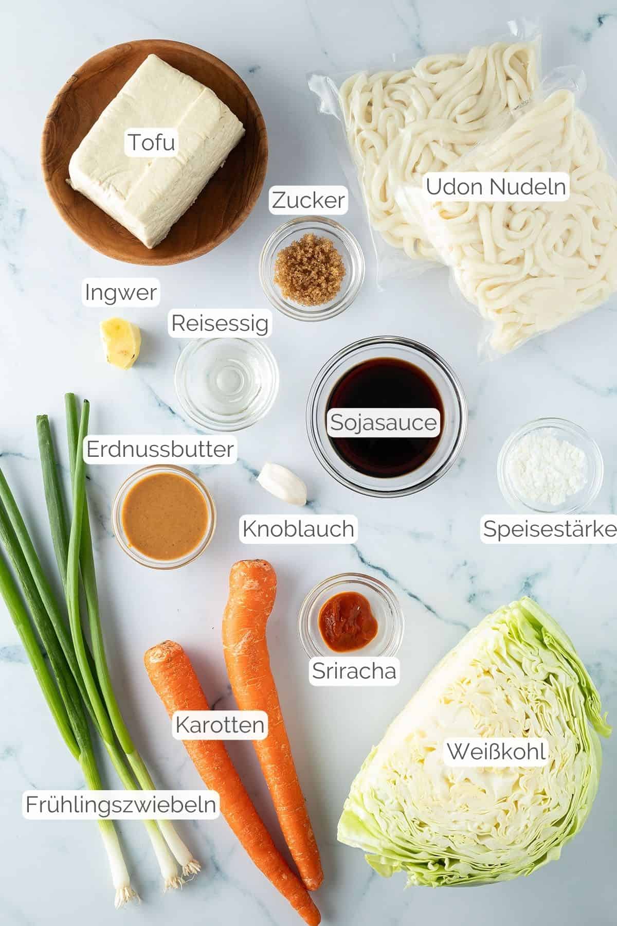 Alle Zutaten mit Textbeschriftungen, die für die gebratenen Udon Nudeln mit Tofu benötigt werden.