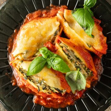 Mit Spinat Ricotta und Thunfisch gef&uuml;llte Muschelnudeln auf einem Teller mit Tomatensauce und frischem Basilikum.