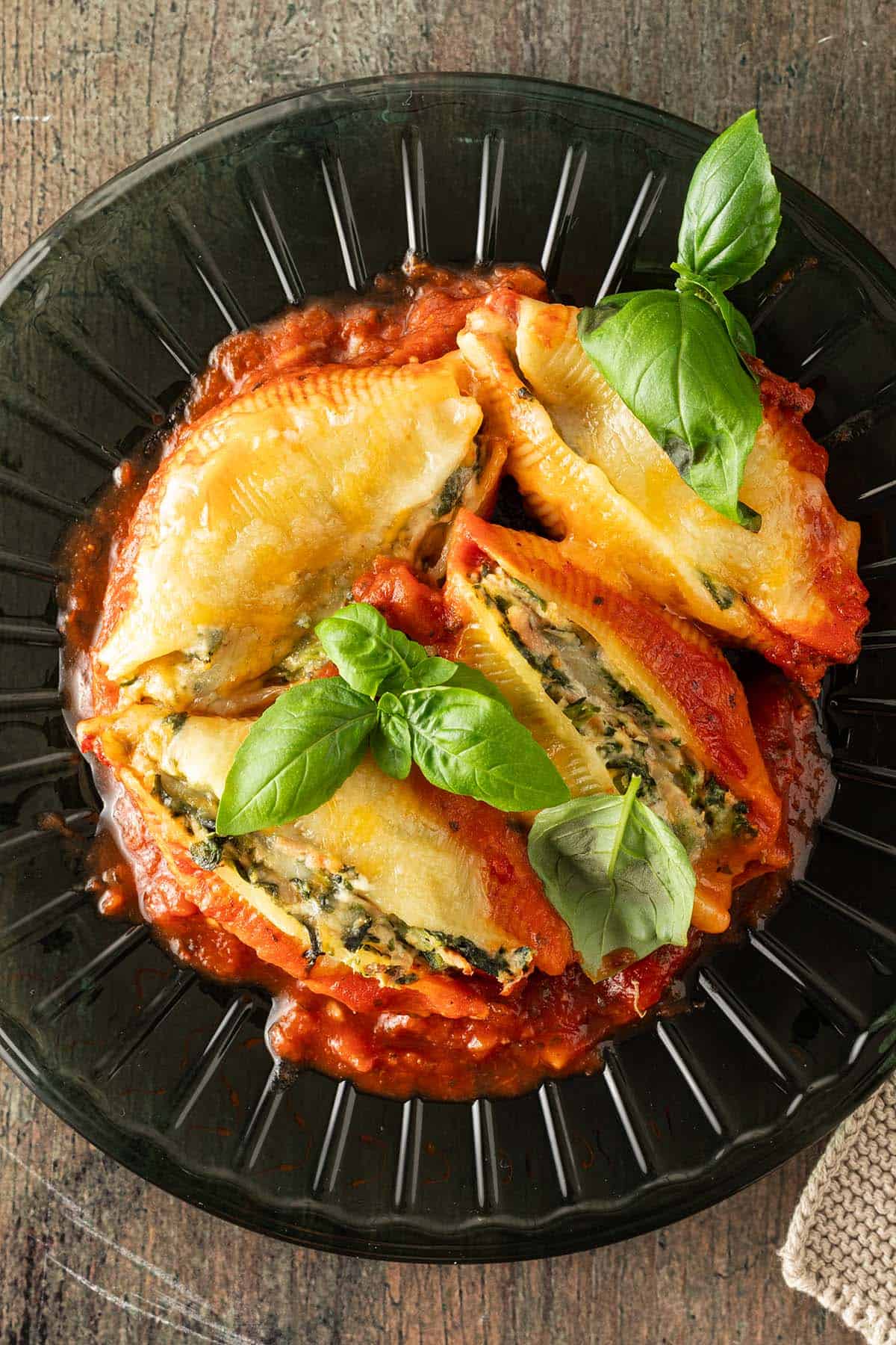 Mit Spinat Ricotta und Thunfisch gef&uuml;llte Muschelnudeln auf einem Teller mit Tomatensauce und frischem Basilikum.