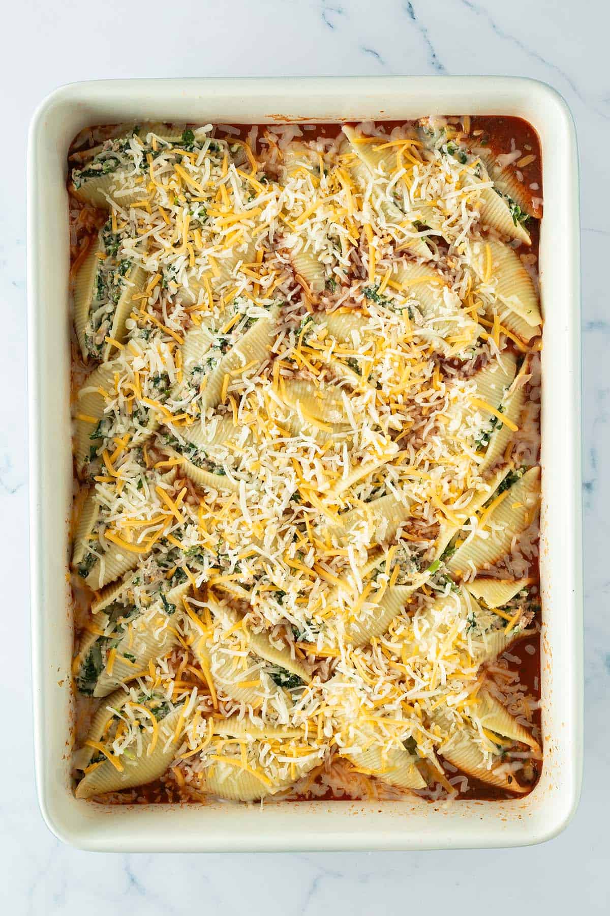 K&auml;se wurde &uuml;ber mit einer Spinatf&uuml;llung gef&uuml;llte Muschelnudeln in einer Auflaufform mit Tomatensauce gestreut.