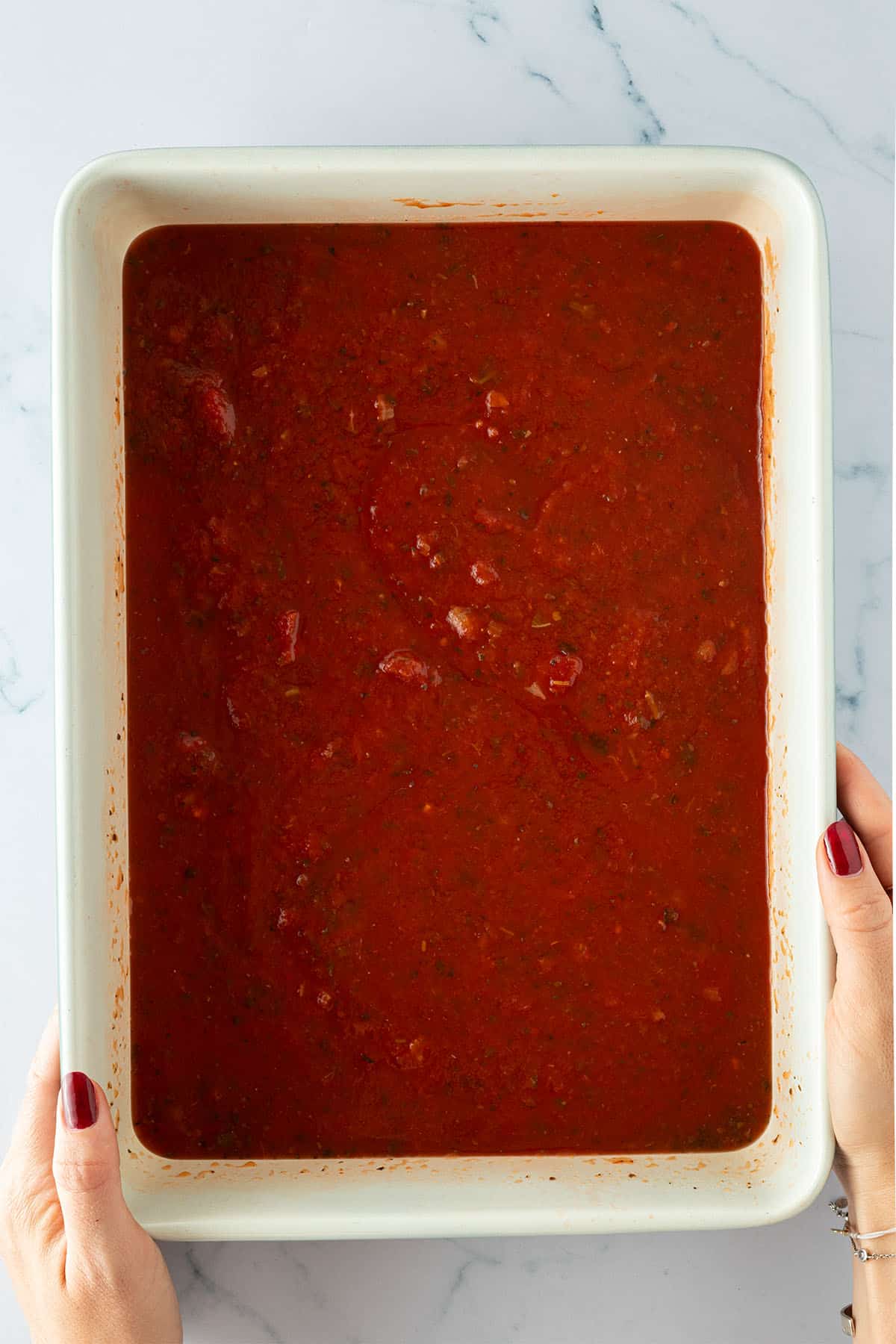 Eine Person h&auml;lt eine gro&szlig;e, rechteckige Auflaufform mit Tomatensauce in den H&auml;nden.