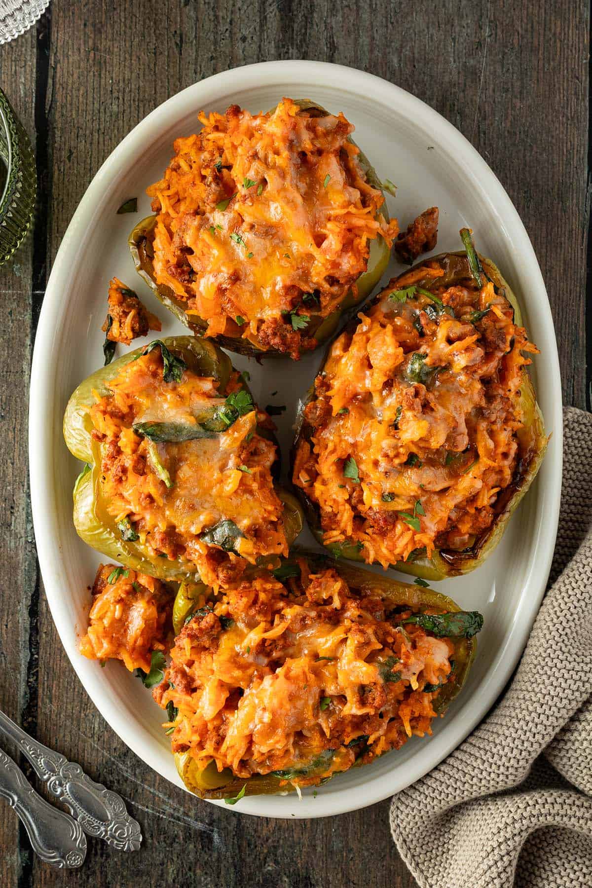 Vier mit Hackfleisch und Reis gef&uuml;llte und mit K&auml;se &uuml;berbackene Paprika-H&auml;lften auf einem ovalen Servierteller.