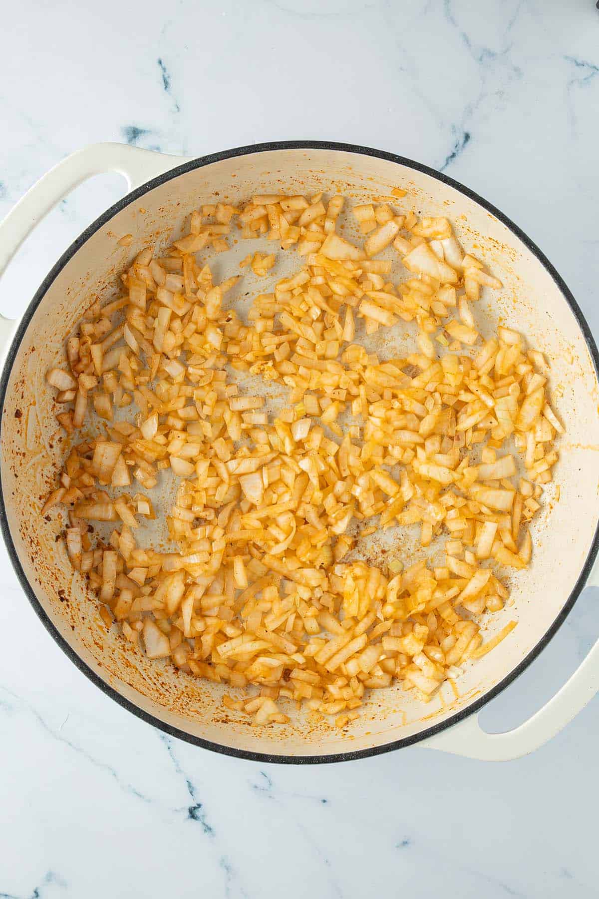 Angebratene Zwiebel- und Knoblauchw&uuml;rfel in einer Pfanne.
