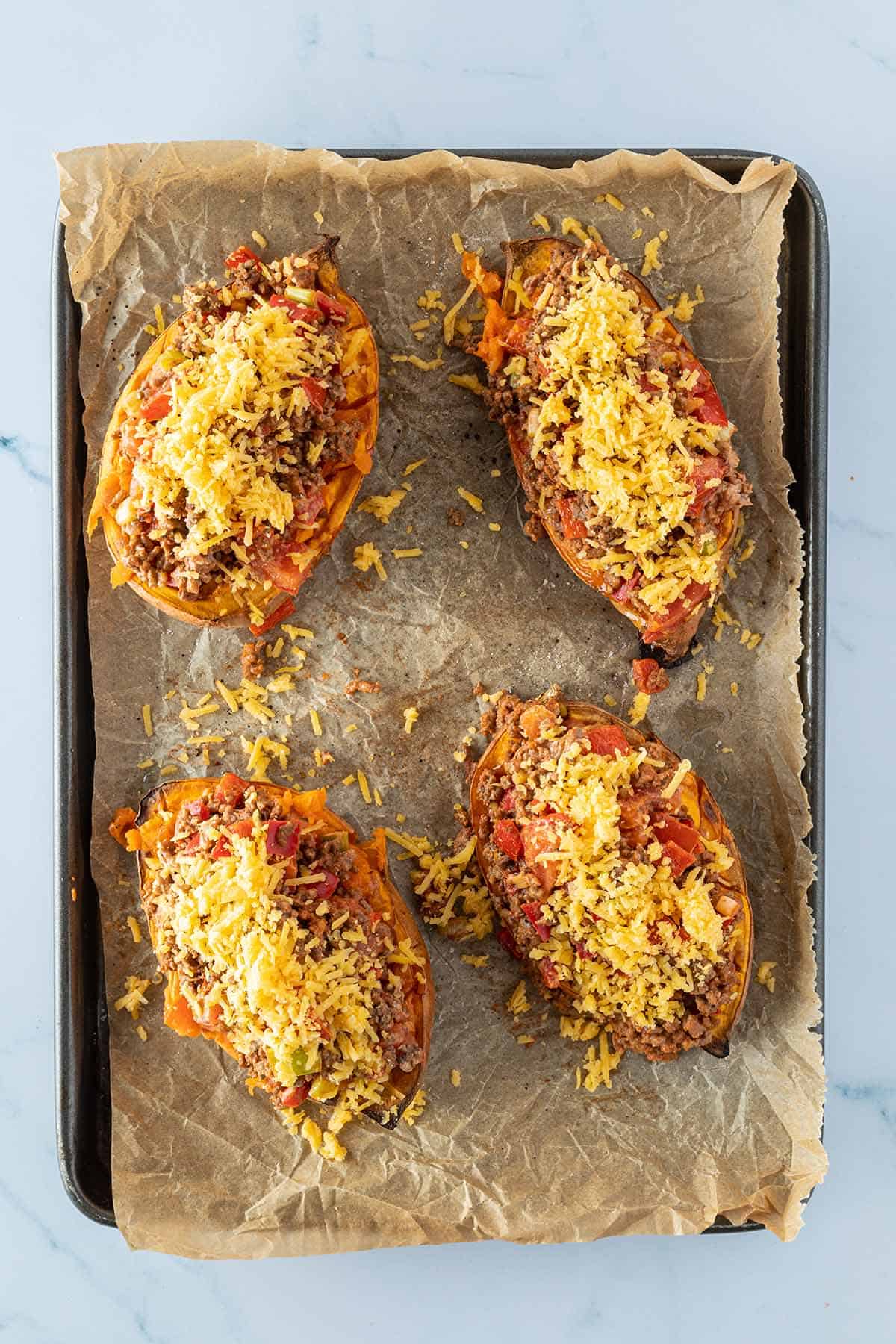 Vier mit Hackfleisch und Käse gefüllte Süßkartoffelhälften auf einem Blech.