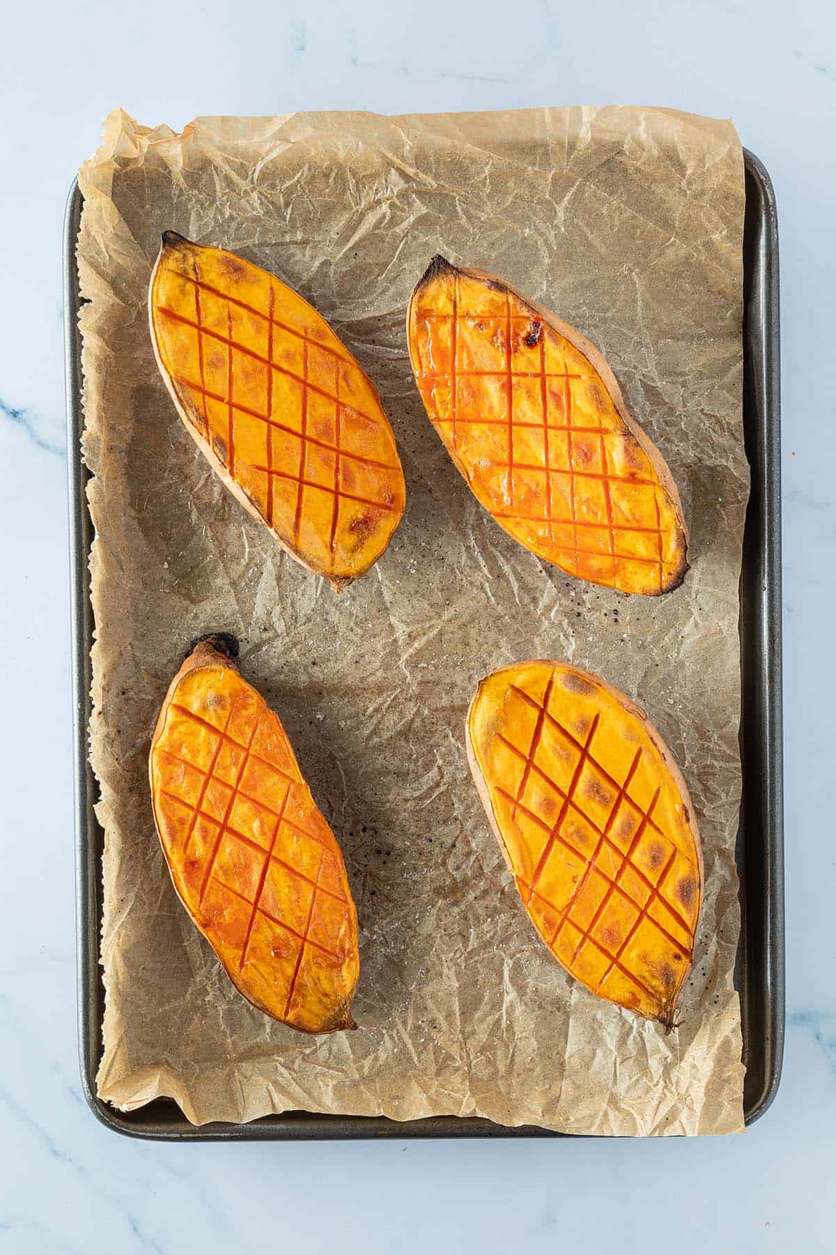 Vier weich geröstete Süßkartoffelhälften auf einem Backblech.