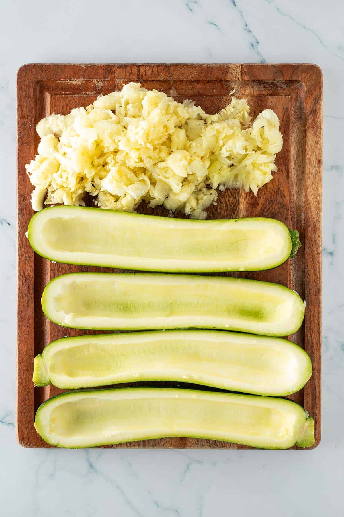 Ausgeh&ouml;hlte Zucchinih&auml;lften und das entfernte Fruchtfleisch auf einem Holzbrett.