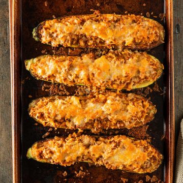 Vier gef&uuml;llte Zucchinih&auml;lften mit goldbrauner K&auml;sekruste auf einem Backblech aus dem Ofen.
