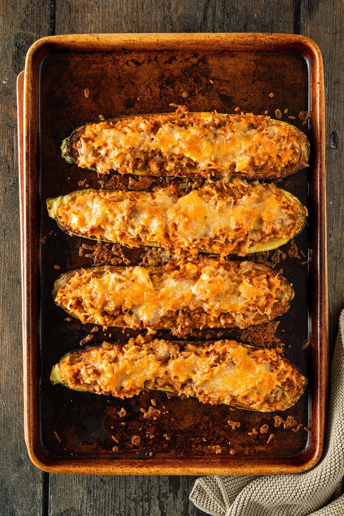 Vier gef&uuml;llte Zucchinih&auml;lften mit goldbrauner K&auml;sekruste auf einem Backblech aus dem Ofen.