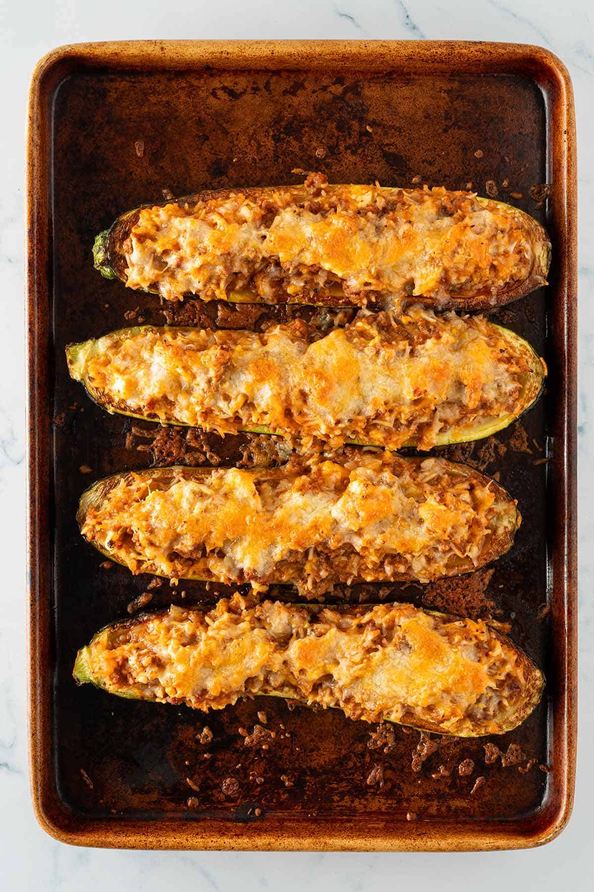 Gef&uuml;llte Zucchinih&auml;lften mit geschmolzenem K&auml;se auf einem Backblech.