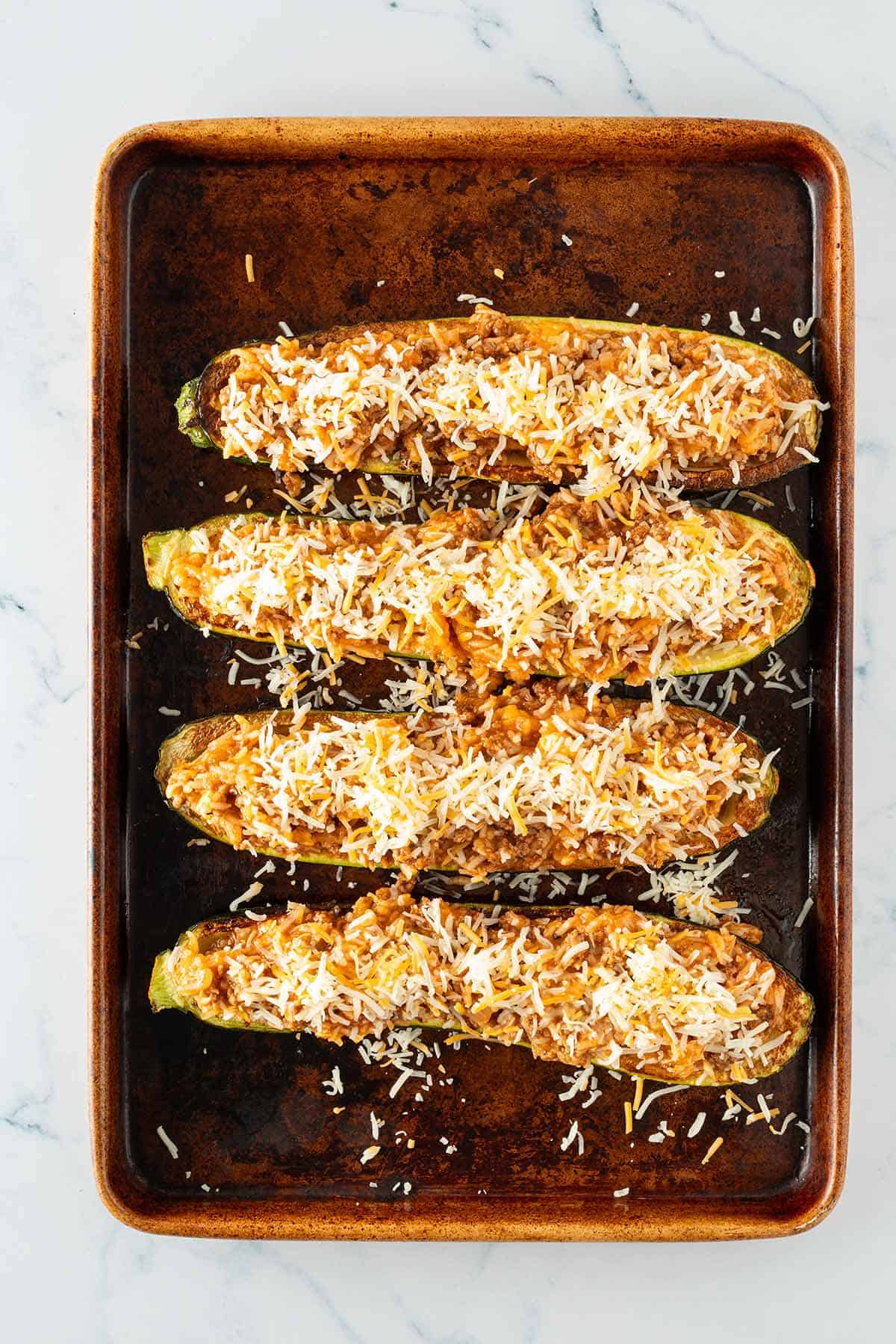 Rohe gef&uuml;llte Zucchinih&auml;lften mit der Reis-Pfanne gef&uuml;llte und geriebenem K&auml;se vor dem Backen auf einem Blech.