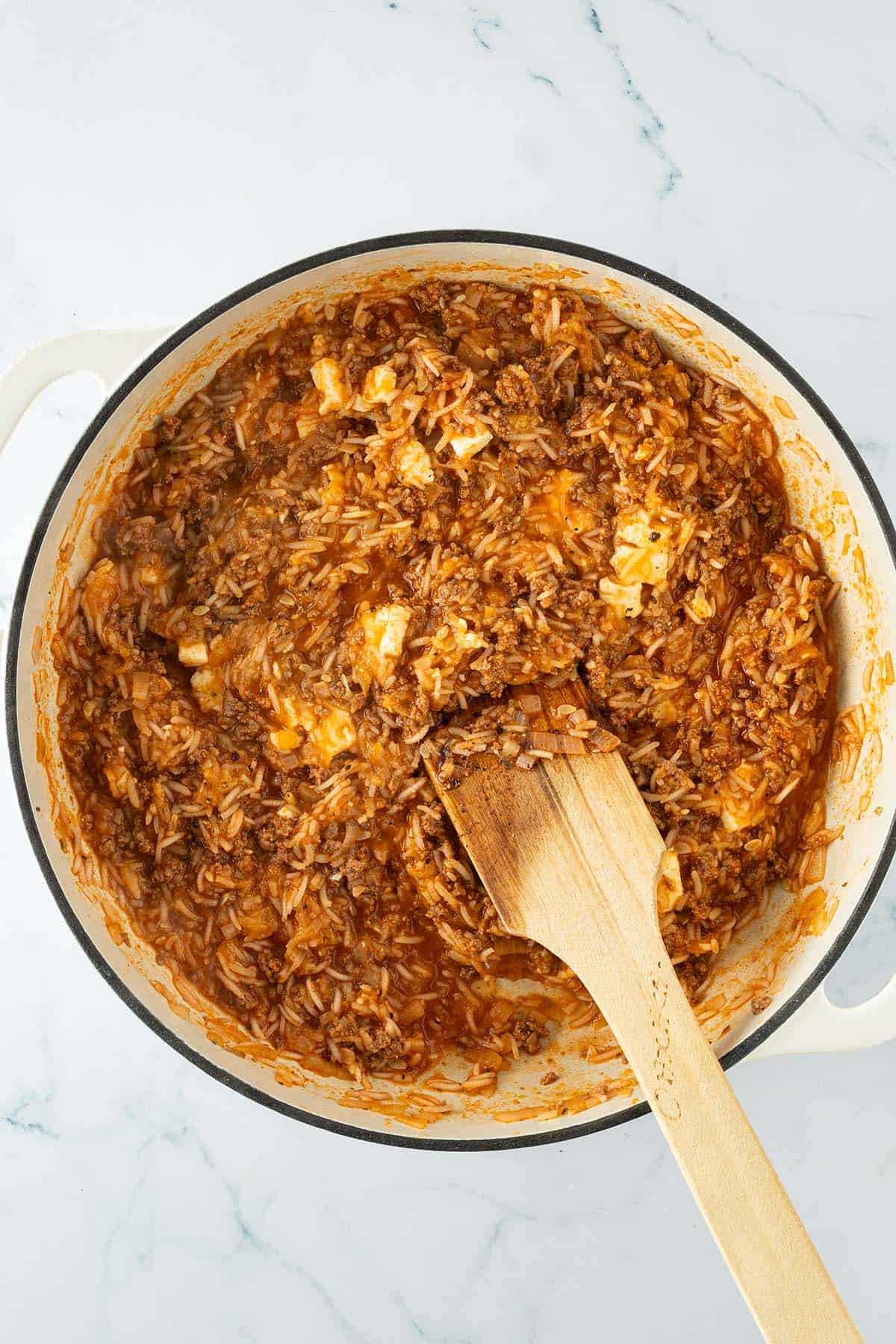 Reis-Hackfleisch-F&uuml;llung mit Tomatenso&szlig;e und Feta in einer Pfanne, mit Holzl&ouml;ffel ger&uuml;hrt.