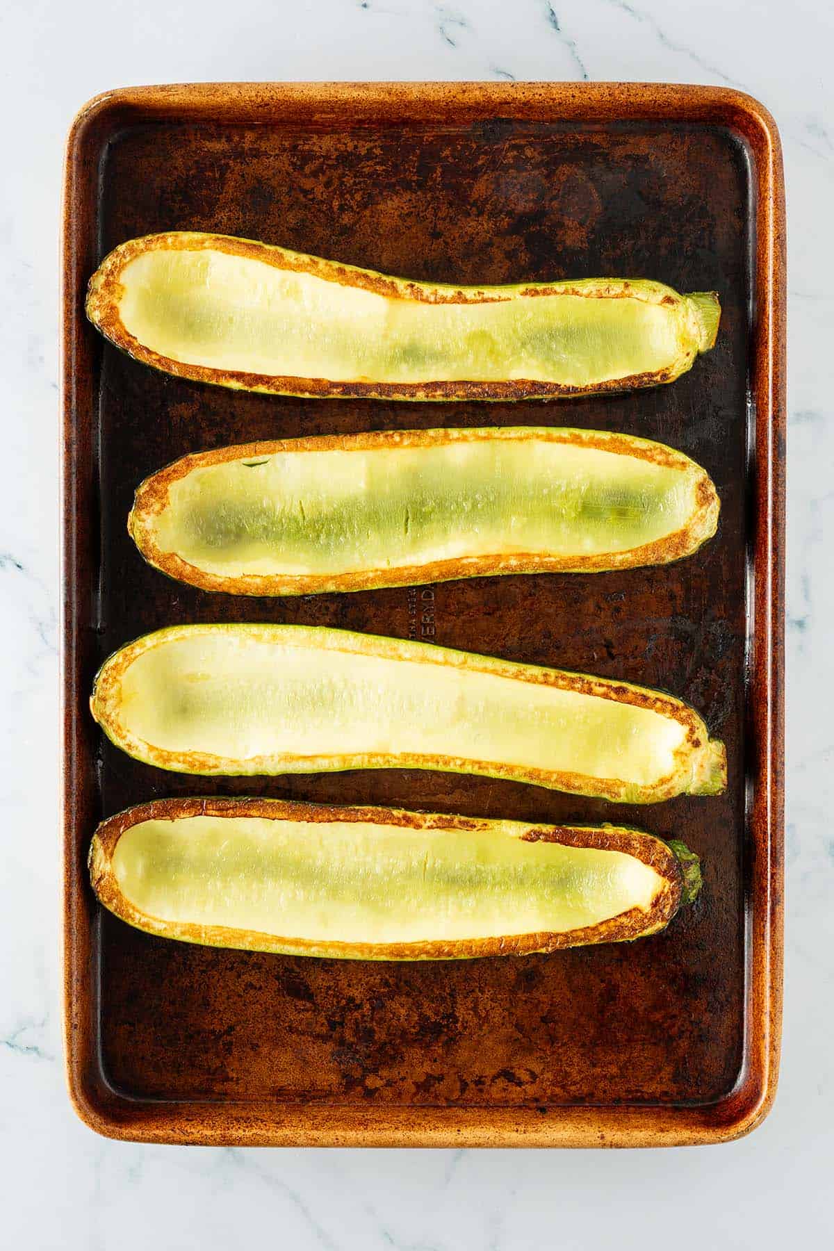 Ausgeh&ouml;hlte und im Ofen ger&ouml;stete Zucchinih&auml;lften auf einem Backblech, bereit zum F&uuml;llen.