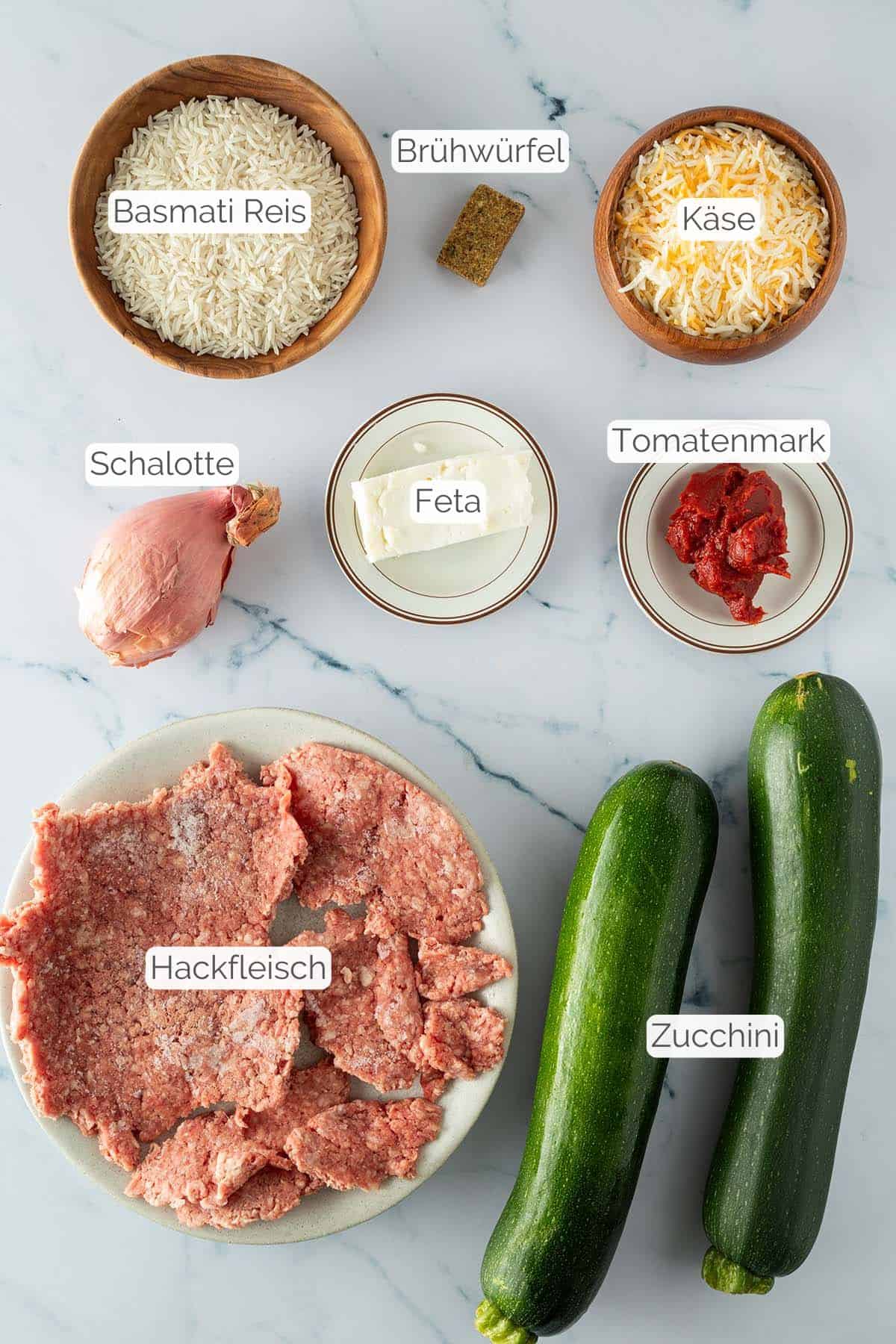 Alle Zutaten mit jeweiligen Textbeschriftungen, die f&uuml;r die gef&uuml;llten Zucchini mit Reis ben&ouml;tigt werden.