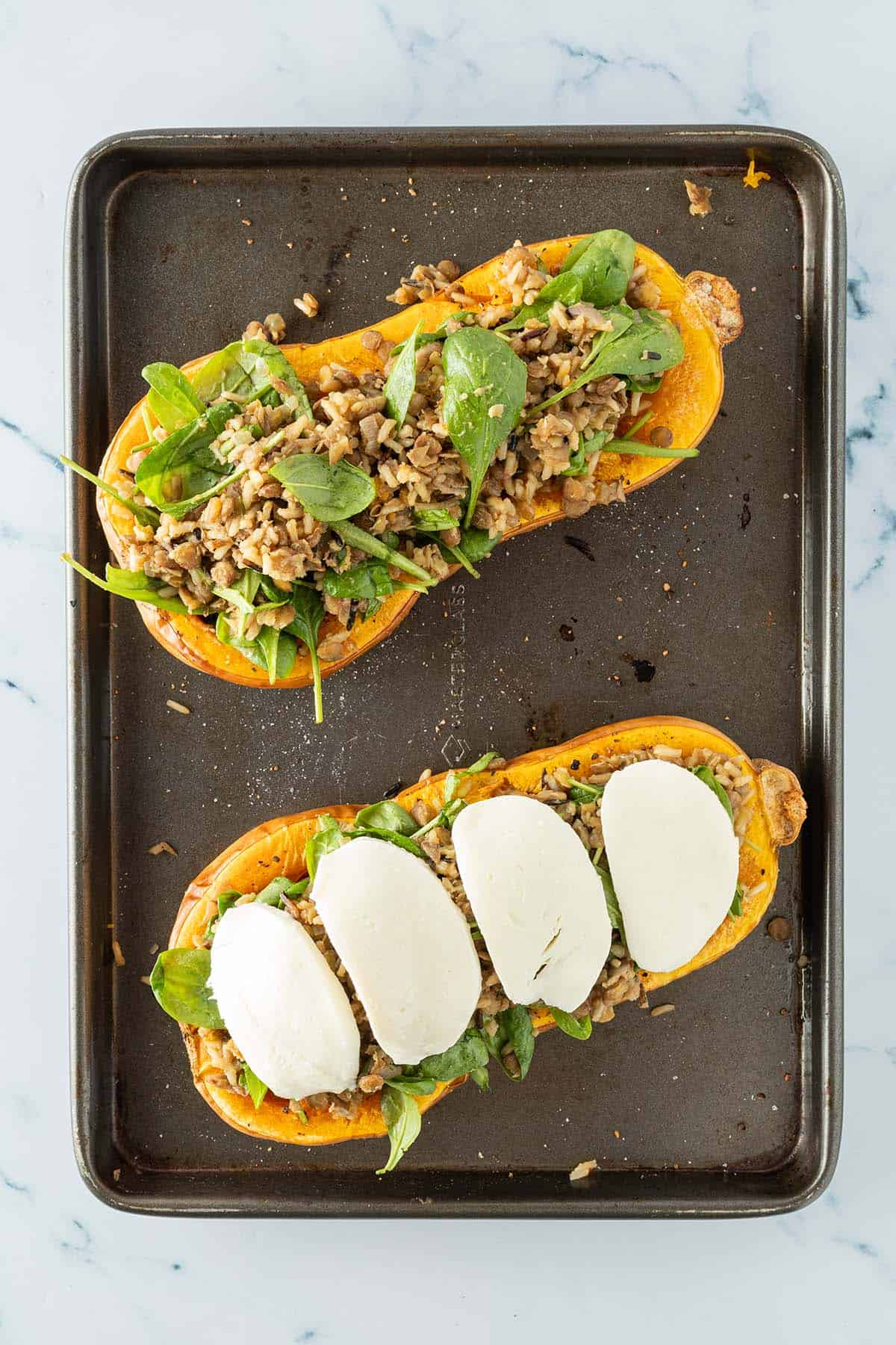 Gef&uuml;llte K&uuml;rbish&auml;lften auf einem Blech, eine davon mit Mozzarellascheiben darauf.