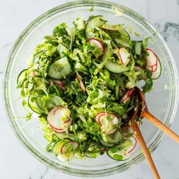 Gemischter Beilagensalat mit Gurken, Salat, Radieschen in einer gro&szlig;en Glassch&uuml;ssel mit Salatbesteck.