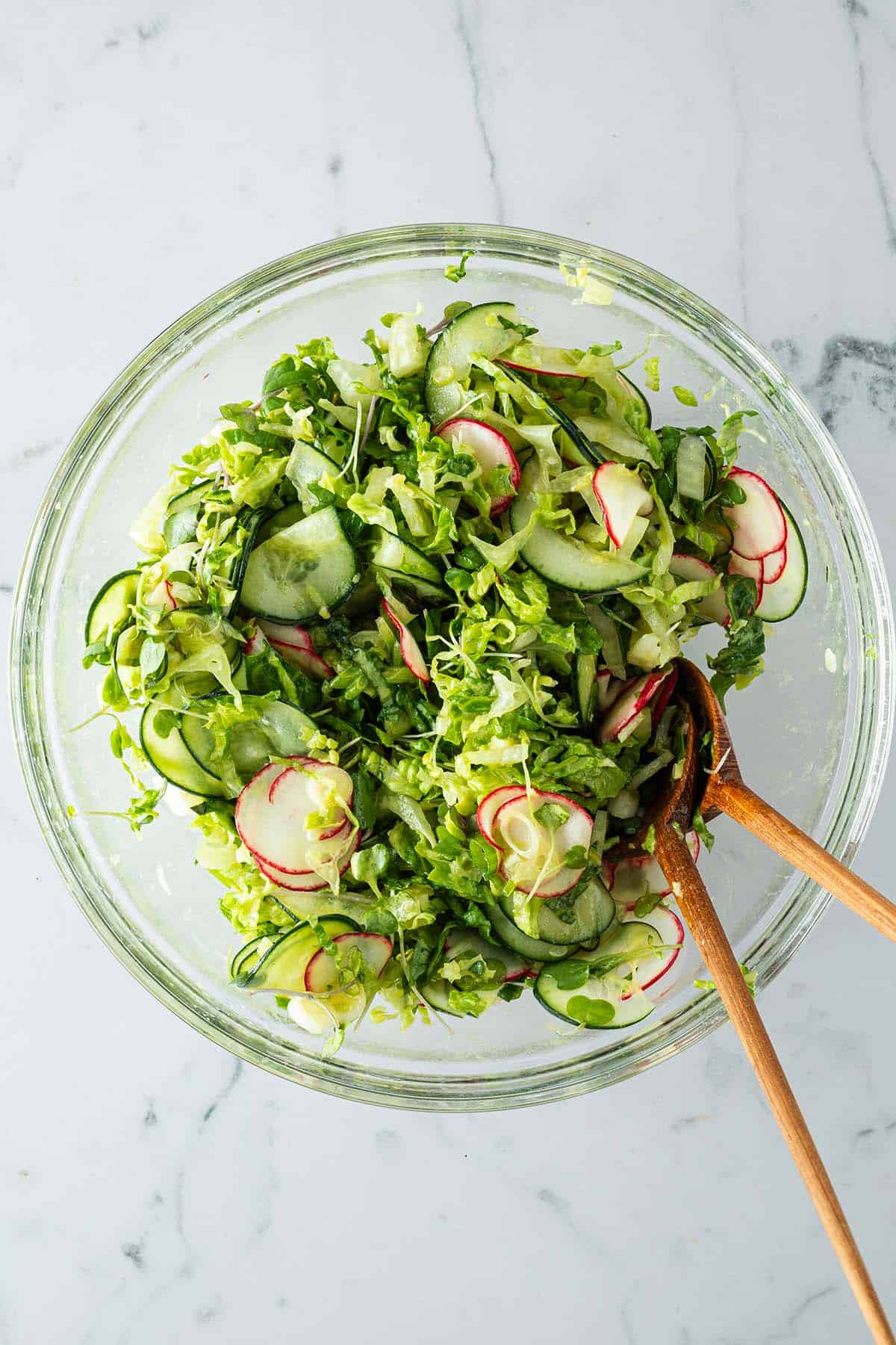 Gemischter Beilagensalat mit Gurken, Salat, Radieschen in einer gro&szlig;en Glassch&uuml;ssel mit Salatbesteck.