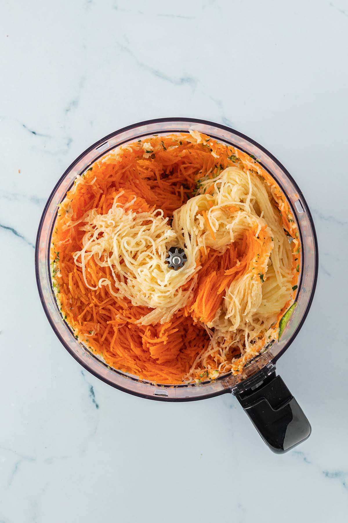 Fein geraspelte Karotten, Kartoffeln und Zucchini in einem Food Processor.