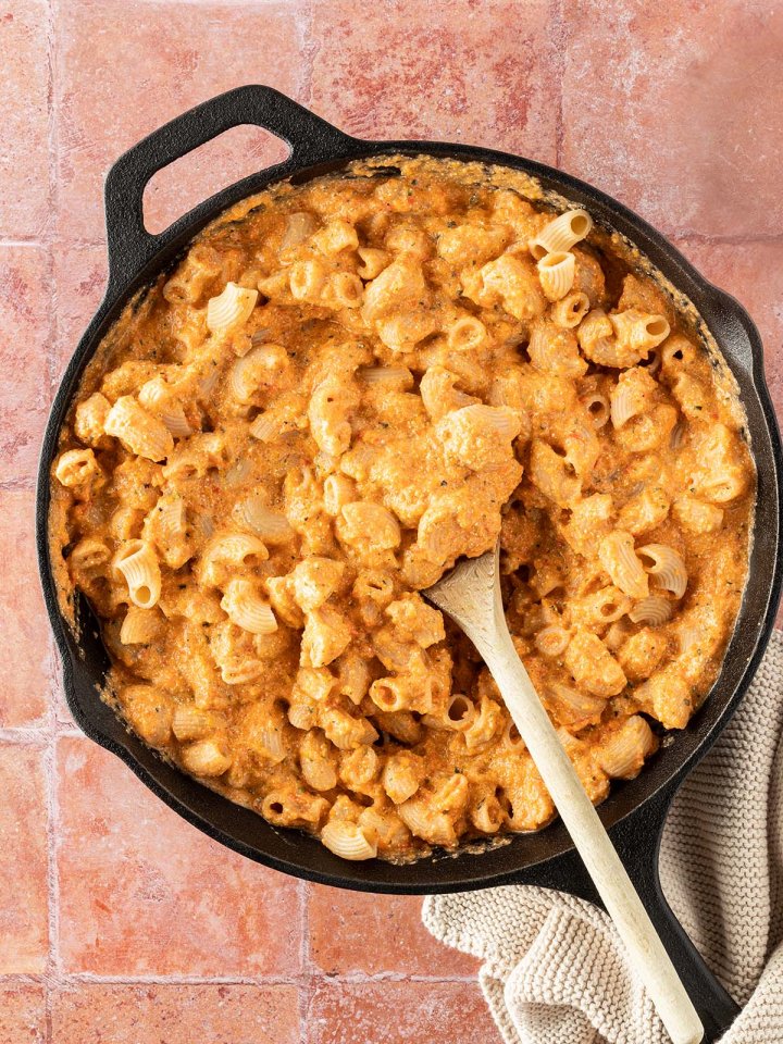 Eine Pfanne mit kurzen Nudeln in einer cremigen K&auml;se-Gem&uuml;sesauce auf einem roten Flie&szlig;enuntergrund.