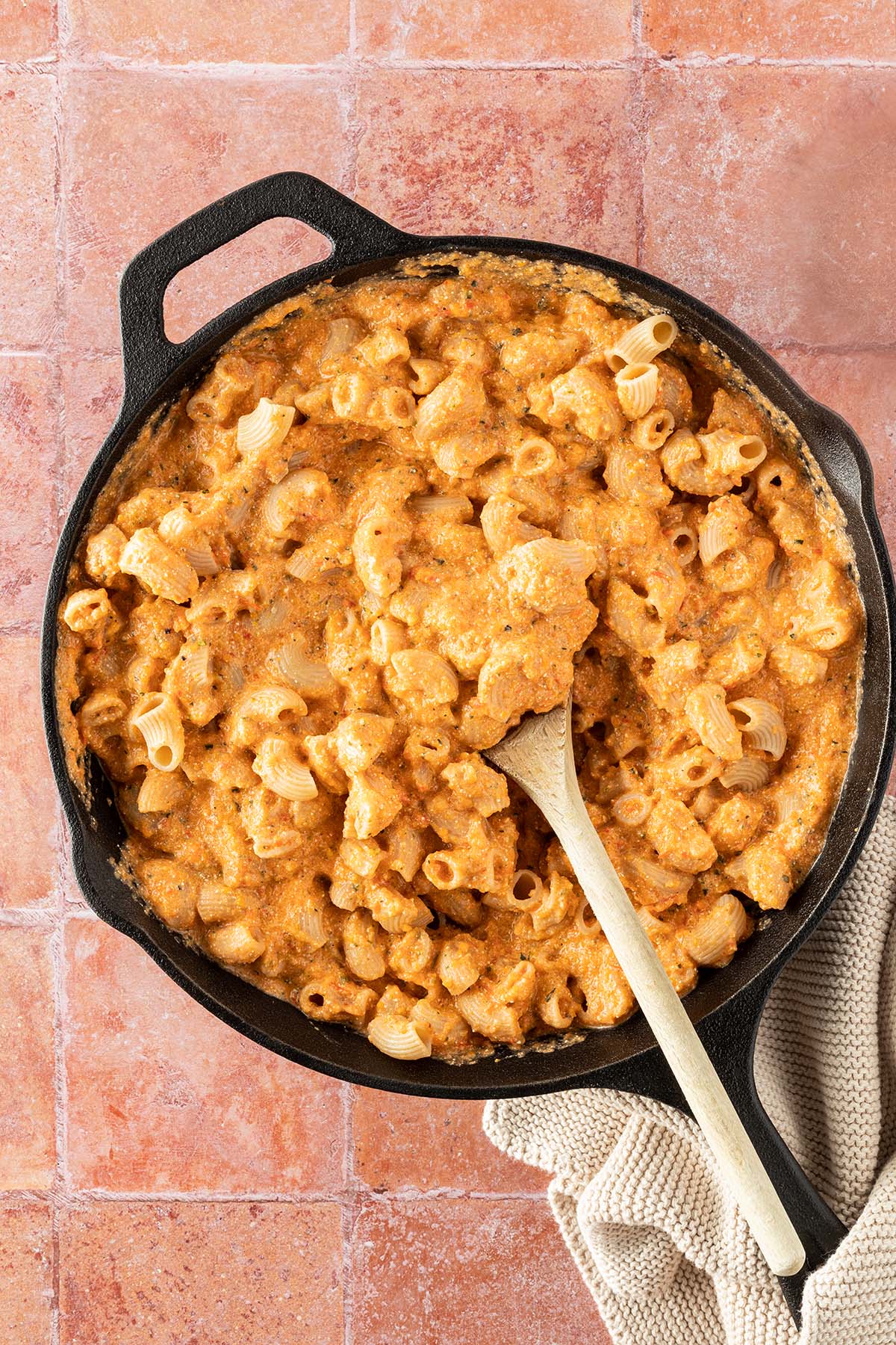 Eine Pfanne mit kurzen Nudeln in einer cremigen K&auml;se-Gem&uuml;sesauce auf einem roten Flie&szlig;enuntergrund.