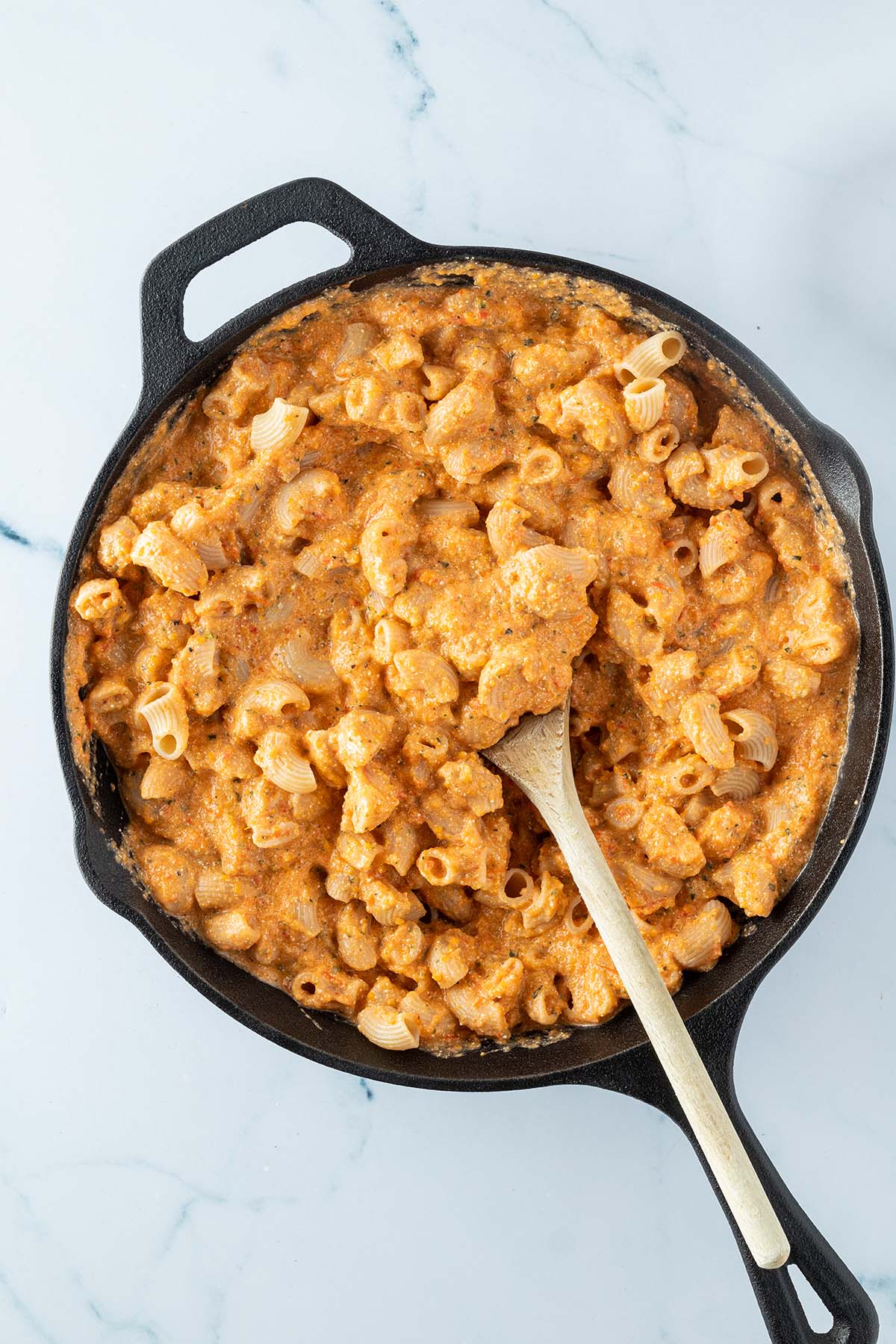 Vogelperspektive auf eine Pfanne, in der die Gem&uuml;sesauce mit kurzen Nudeln vermischt wird.