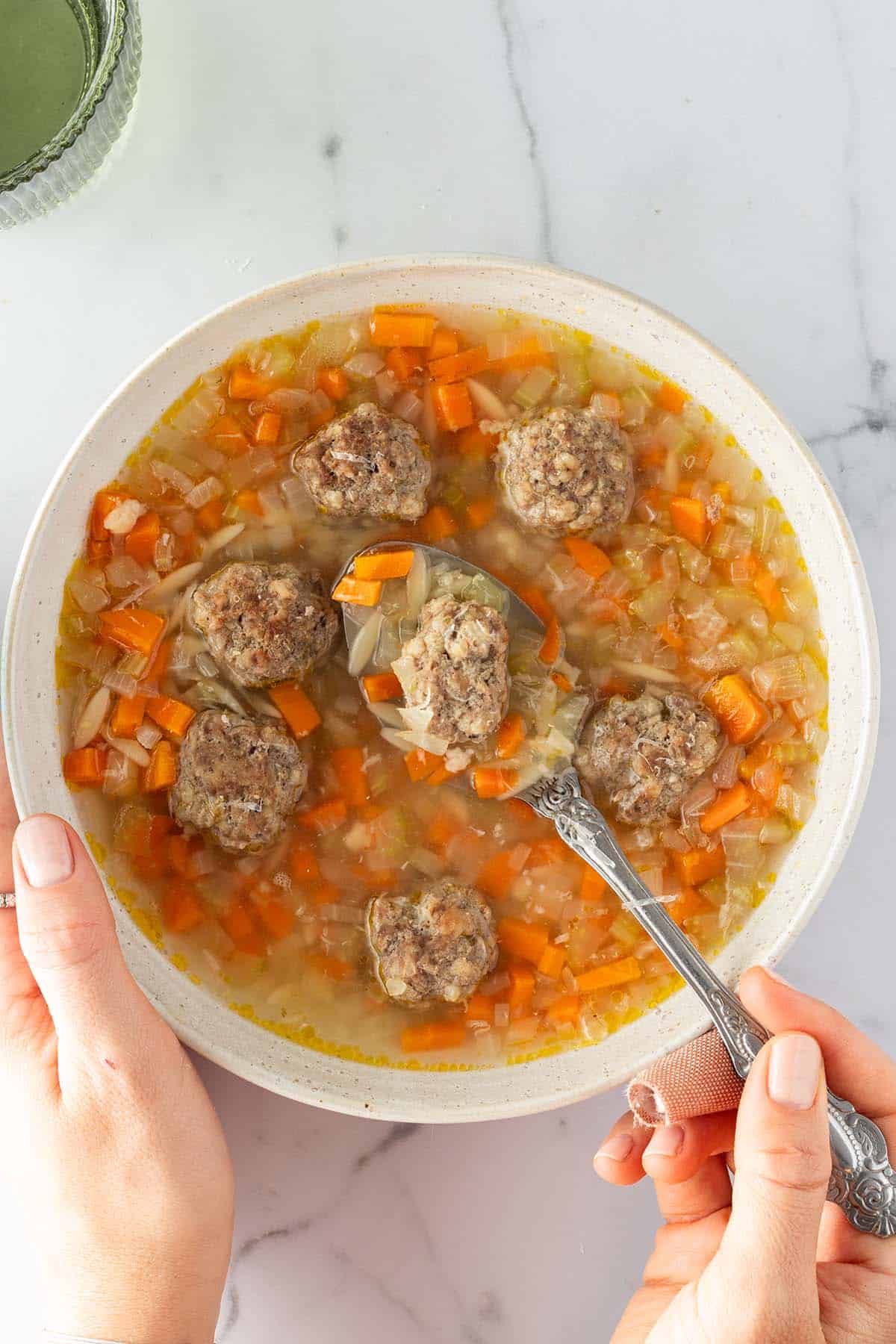 Eine Person h&auml;lt eine Sch&uuml;ssel mit Gem&uuml;sesuppe, Hackb&auml;llchen und Nudeln in der Hand.