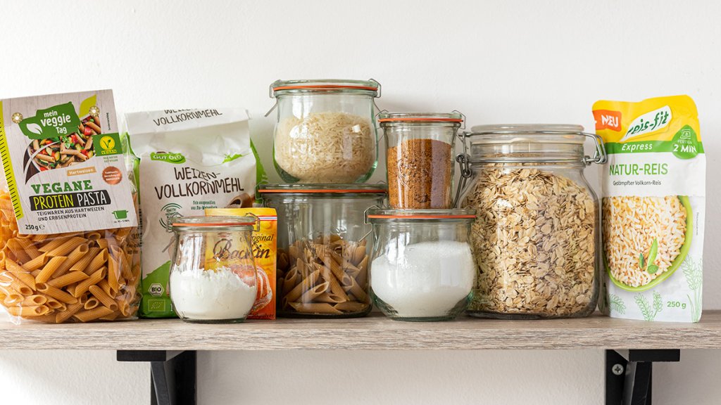 Gesunde Kohlenhydrate f&uuml;r die Vorratskammer: Vollkornnudeln, Mehl, Reis, Haferflocken, kalorienfreie S&uuml;&szlig;e, Kokosbl&uuml;tenzucker, St&auml;rke und Backpulver auf einem Regal nebeneinander aufgereiht.