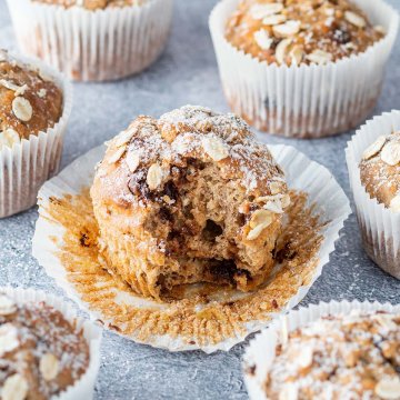 Ein angebissener Muffin auf grauen Untergrund, umgeben von weiteren Muffins.