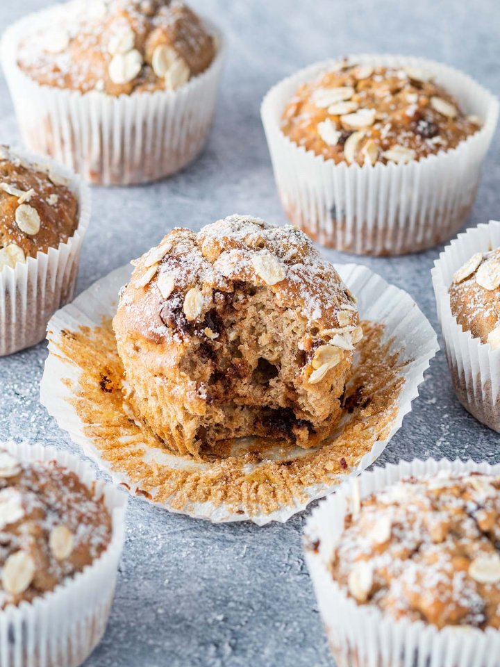 Ein angebissener Muffin auf grauen Untergrund, umgeben von weiteren Muffins.