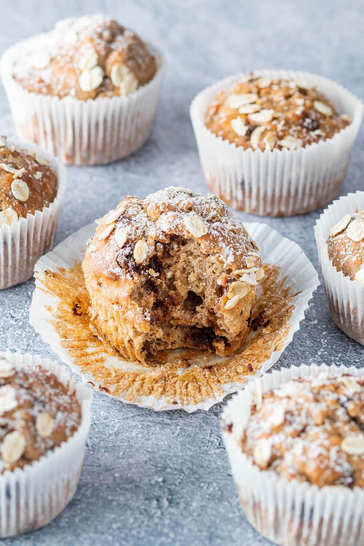 Ein angebissener Muffin auf grauen Untergrund, umgeben von weiteren Muffins.