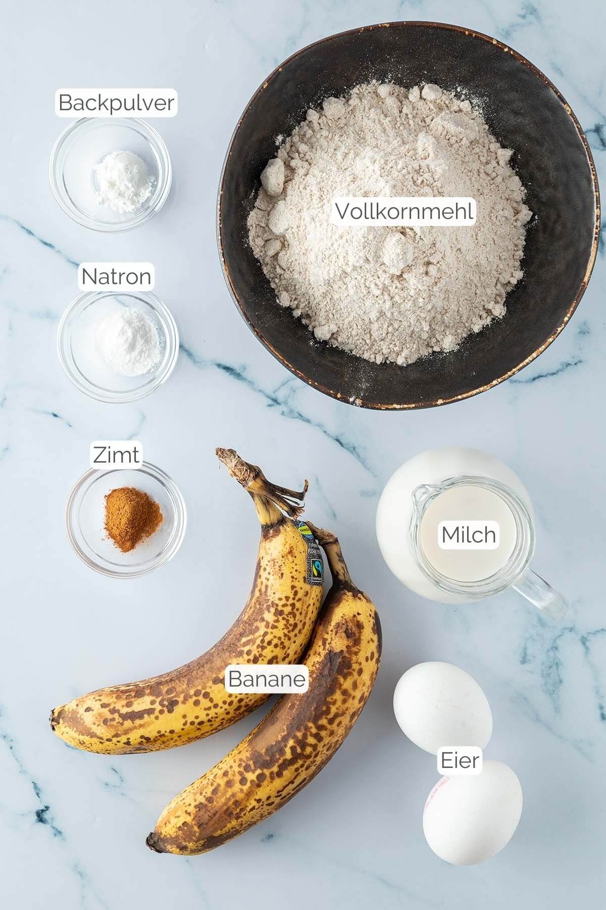 Foto aller Zutaten mit jeweiligen Textbeschriftungen, die f&uuml;r gesunde Bananen Pancakes ben&ouml;tigt werden.