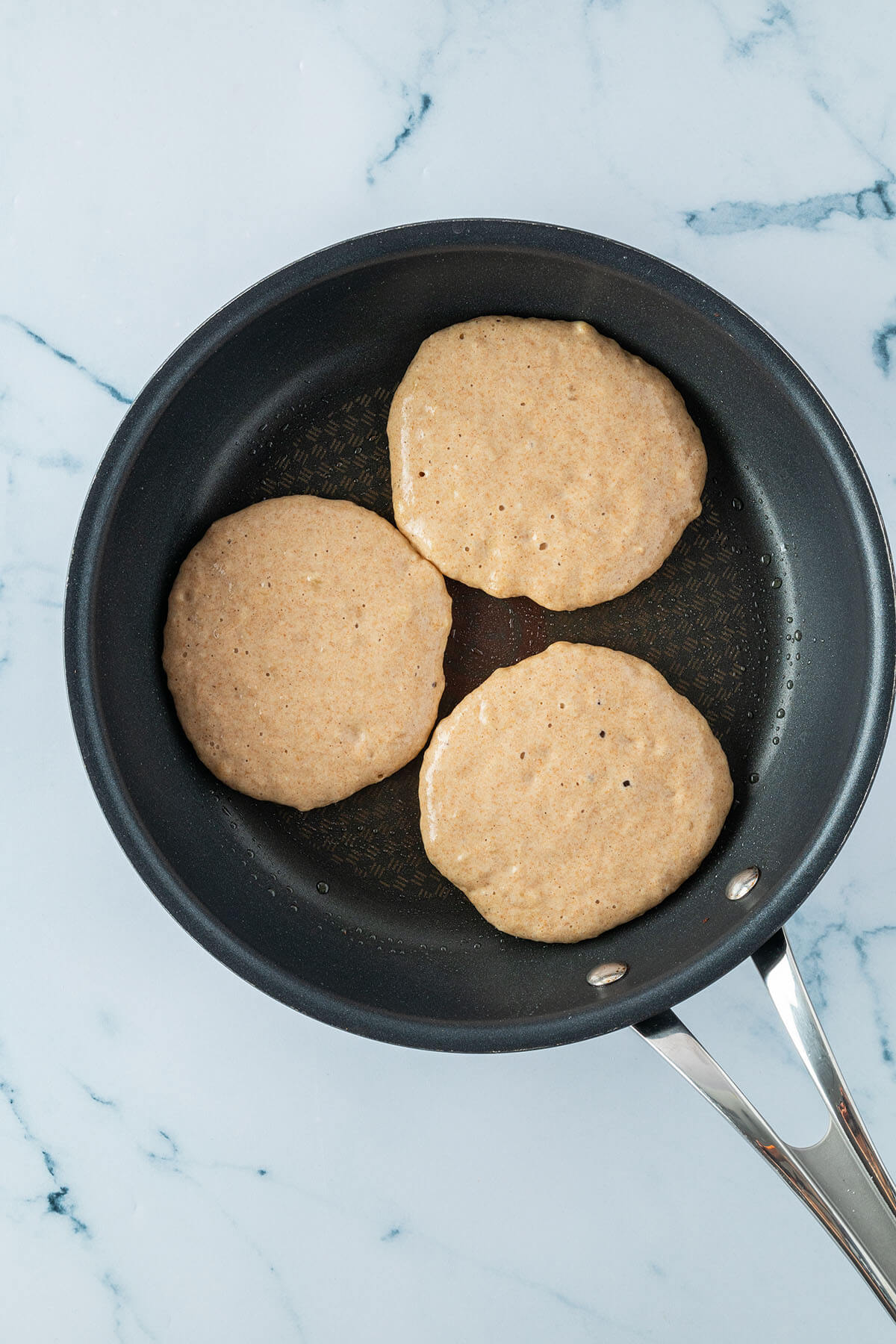 Drei kleine Pancakes in einer Pfanne vor dem Wenden.
